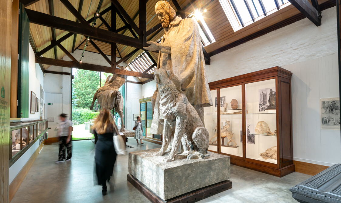 Visitors walk through tall ceiling gallery full of large sculptures