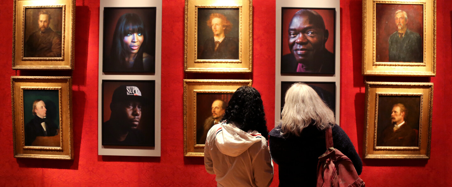 Two visitors look at a portraits hung in the gallery