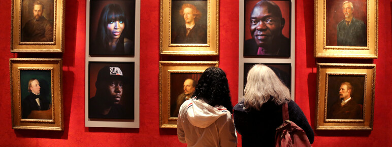 Two visitors look at a portraits hung in the gallery