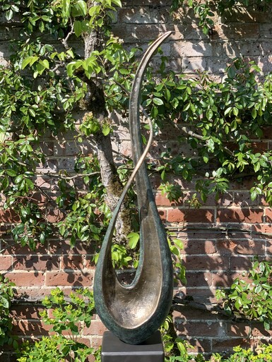 Curved bronze sculpture by Lucy Lutyens set in the outdoors by a red brick wall