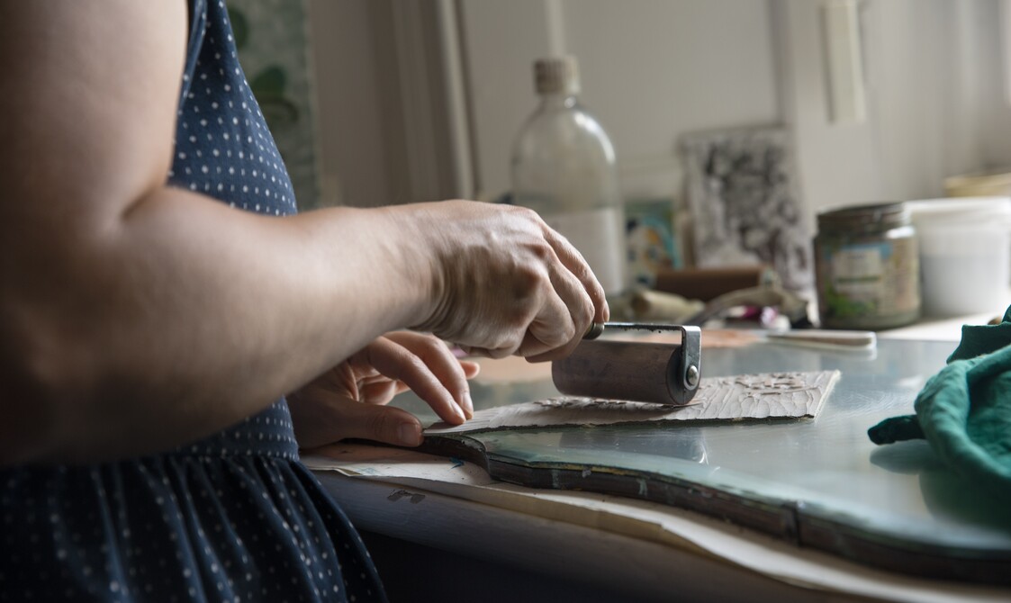 Lisa rolls ink over a piece of lino with a paint roller