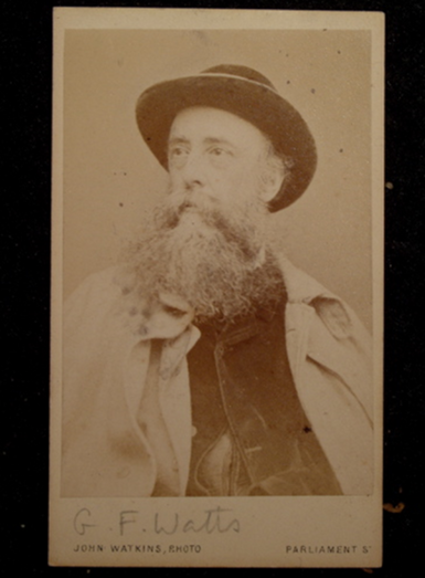 A sepia photo of a middle-aged G F Watts, he has a long beard and wears a wide brimmed hat. He looks to the side of the camera.