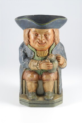 A Toby figure of a crouched man holding a jar and wearing a large brimmed black hat