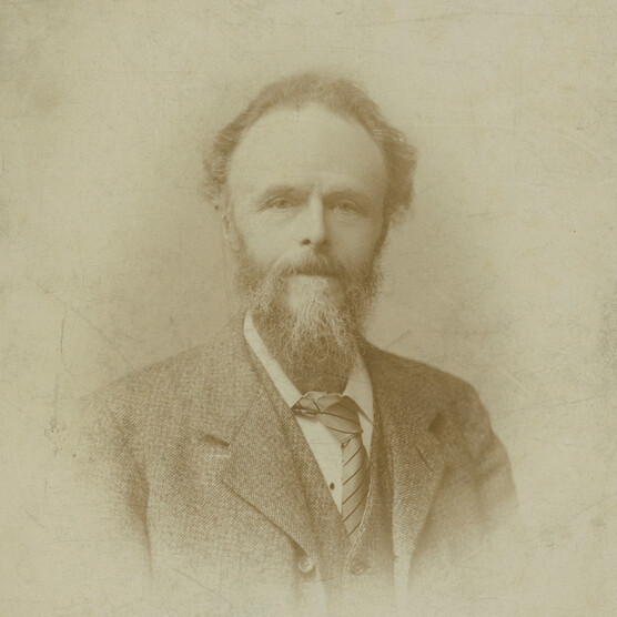 A photo portrait of William De Morgan. He is bearded and wears a suit