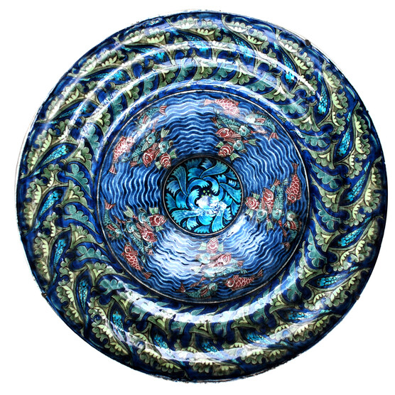 Tin glazed earthenware wide rimmed rice dish. In this intricately patterned dish red and green fish swim in swirling seas around a central petal boss. A seaweed pattern adorns the rim.