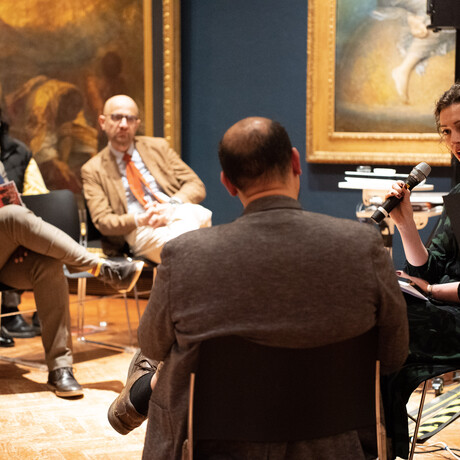 A photograph of curator Emily Burns and composer Des Oliver sitting in the Historic Galleries holding microphones talking