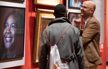 A photograph of two men smiling looking at portraits hung on the wall in the Historic Galleries