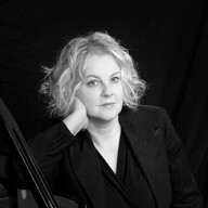 A black and white photograph of a women with blonde hair, leaning on her hand looking at the camera