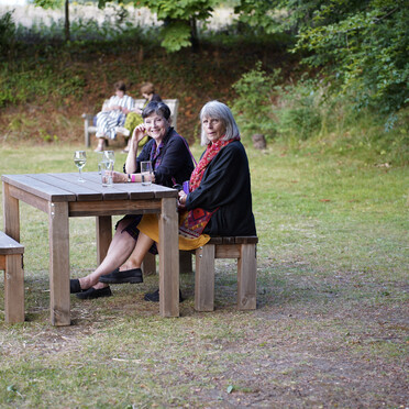 A photograph of two women sitting on a bench outside together looking at the camera smiling
