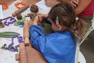 A photograph of a little girl in a blue apron carving into clay during a workshop at Watts Gallery