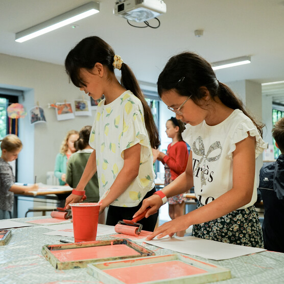 Two girls rolling out pink paint with rollers in a printmaking workshop