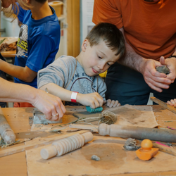 A young boy making with clay, surrounded by parents and other children taking part in the workshop.
