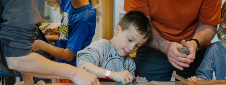 A young boy making with clay, surrounded by parents and other children taking part in the workshop.