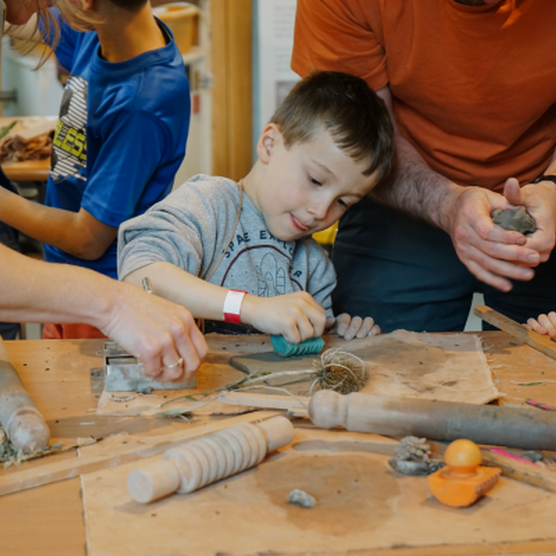 A young boy making with clay, surrounded by parents and other children taking part in the workshop.