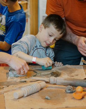 A young boy making with clay, surrounded by parents and other children taking part in the workshop.