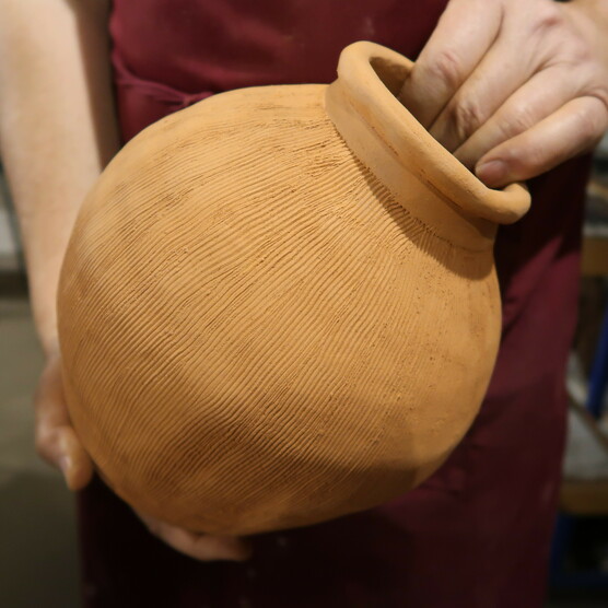 Someone holds a large round clay pot