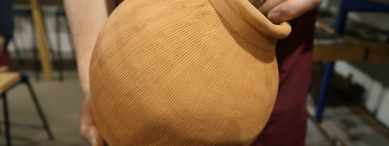 Someone holds a large round clay pot