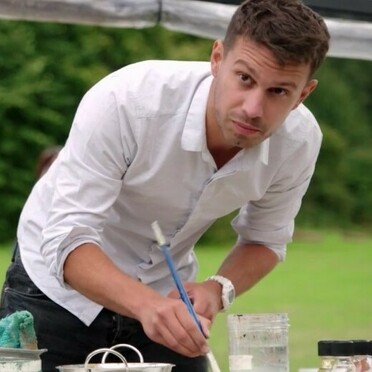 Tom Voyce looks up with a face of concentration, he bends over a desk, holding a paintbrush