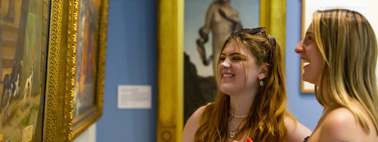 Two young women chat while they look at paintings in the Historic Gallery