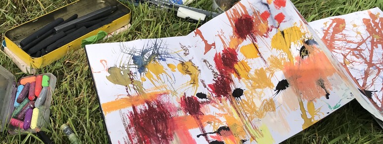 A photograph of paints, paper and tools laid out on grass