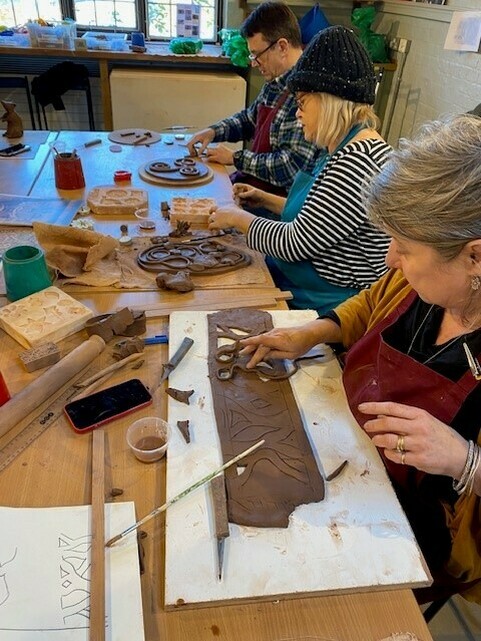 A group of adults working at a table with clay using different tools to carve and shape the clay