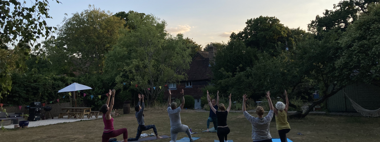 Yoga students hold poses on mats within woodland gardens during sunset