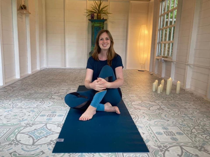 Susie, the yoga instructor sits on a yoga mat with her legs crossed smiling