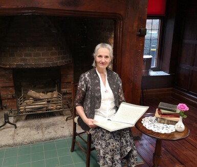 Actor Rowan Suart sitting in front of an open fireplace on a chair reading a book