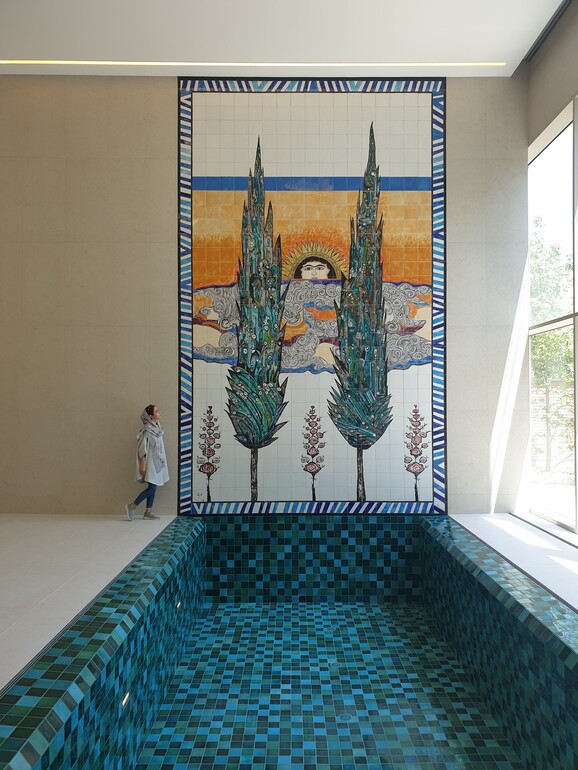 A large ceramic mural connected to a swimming pool. The mural has green tall tress and a face like the sun shining through the trees.