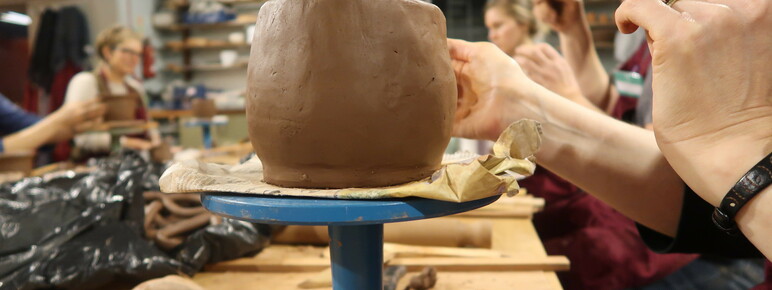 A close up of a clay pot on a blue stand at a pottery workshop