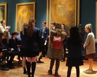 Group of school children in school uniform standing in an art gallery having a discussion. Some of the children are sitting on a bench.
