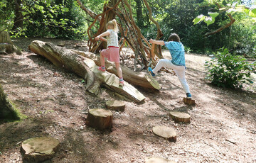 Two children leap over some logs in the Playwood