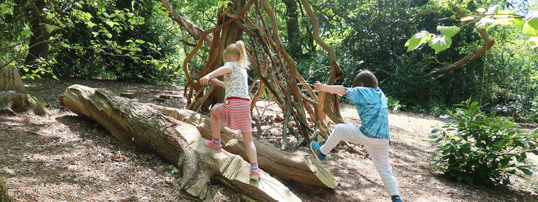 Two children leap over some logs in the Playwood