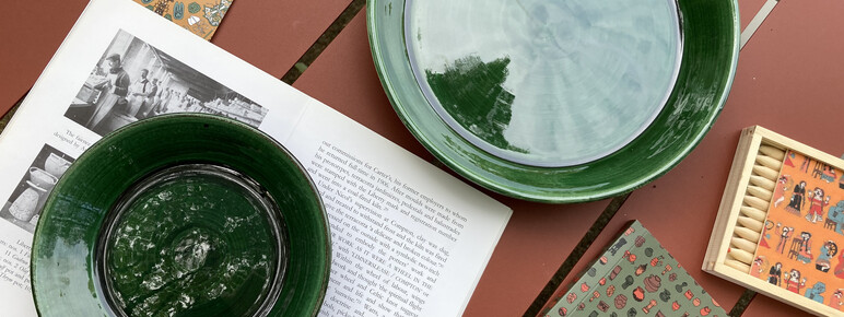 A green plate and bowl, a notebook and a set of colouring pencils are arranged across a terracotta background