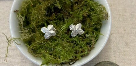 Photo of a bowl with moss in, with a pair of silver stud earrings and a ring placed in the moss which resemble flowers