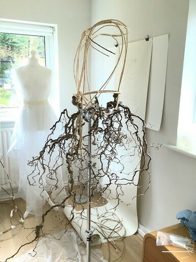 Photo of a wire mannequin with a skirt accessory wrapped around it. The accessory resembles a bunch of twigs.