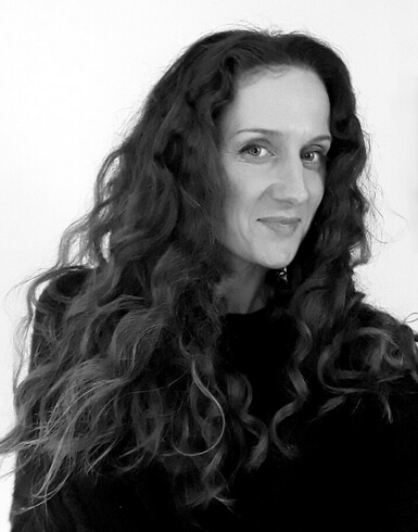 Black and white photo of a woman with long dark curly hair, smiling at the camera