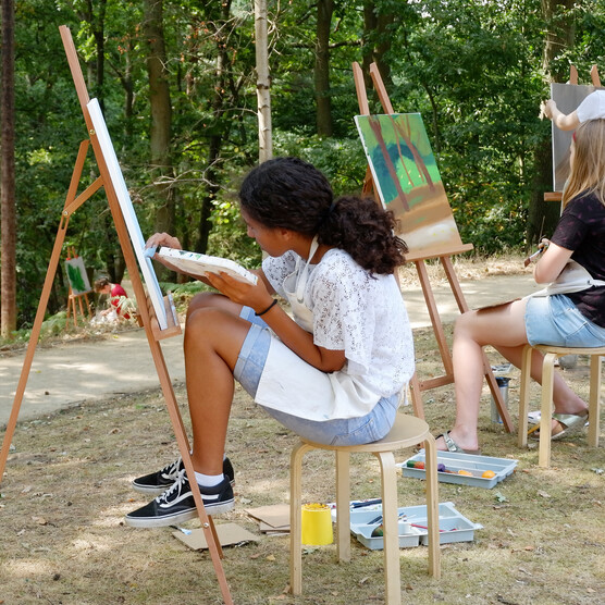 Two girls sit painting at easels outside Limnerslease