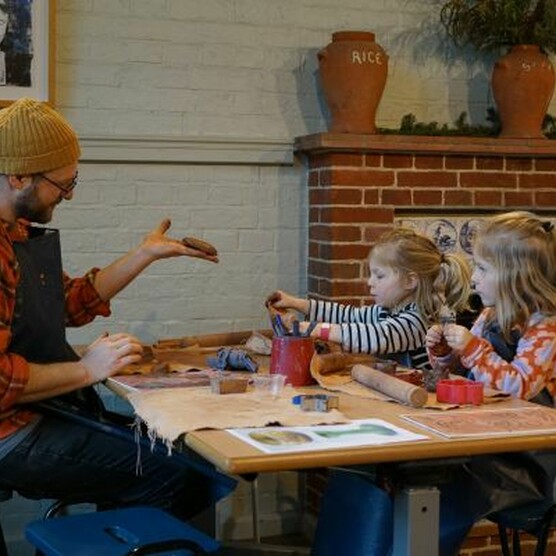 A dad sat down at a table with his two daughters wearing aprons creating with clay