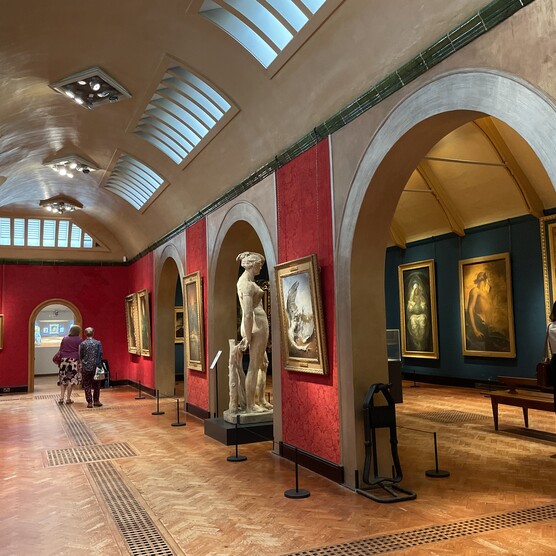 The gallery has red walls and a wooden slatted floor. There is a wall with three arches through which there is another room