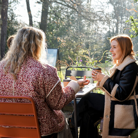 Three people sitting outside at a table, drinking hot drinks and chatting.