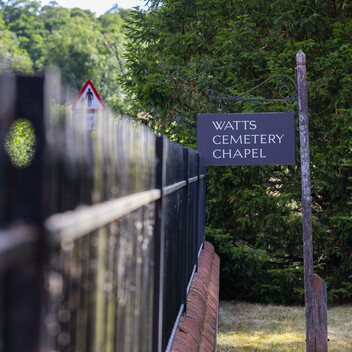 A simple slate sign with white writing says: Watts Cemetery Chapel