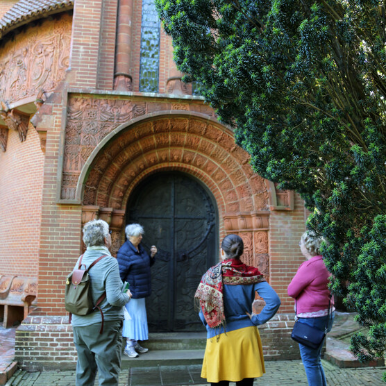 A group of four gather around the detailed black Watts Chapel door