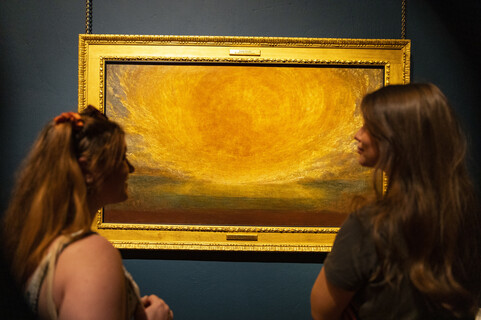 Two visitors look at each other in front of painting of sun