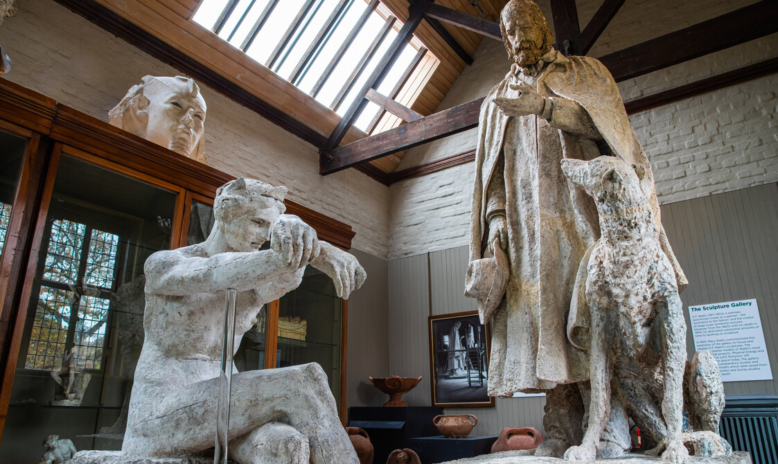 Plaster model of a women in foreground, with Alfred Lord Tennyson statue in background, featuring a man and dog