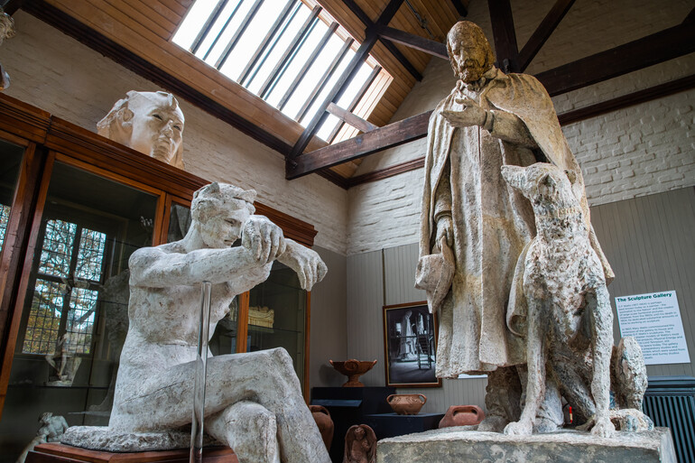Plaster model of a women in foreground, with Alfred Lord Tennyson statue in background, featuring a man and dog