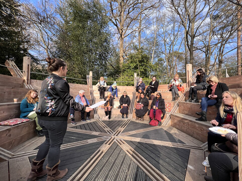 A group of people sit on the wooden round amphitheatre