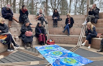 Visitors gather on wooden auditorium looking at painted fabric on the ground