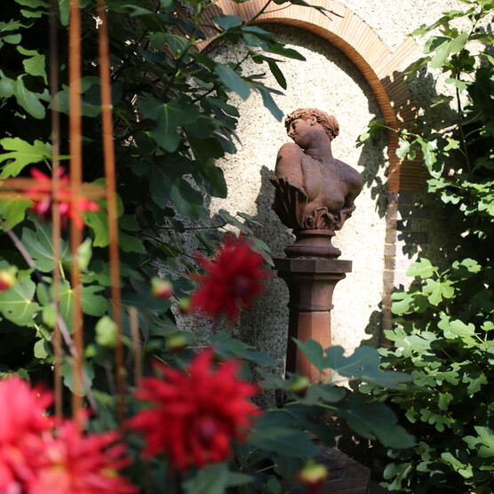 Terracotta bust of a women turning her head, outside surrounded by bright pink flowers
