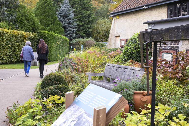 Two visitors walk along the path with flower beds next to them